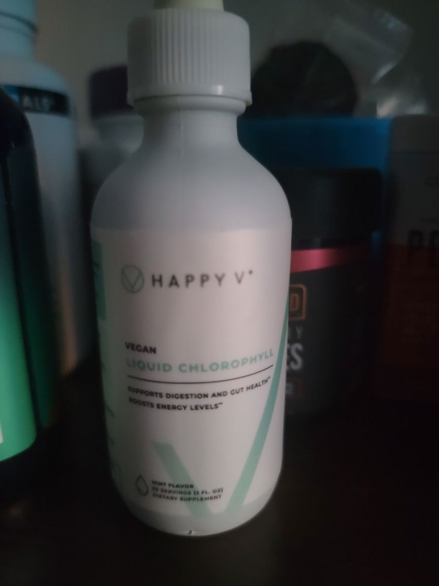 A closeup of a Happy V Liquid Chlorophyll bottle next to other products