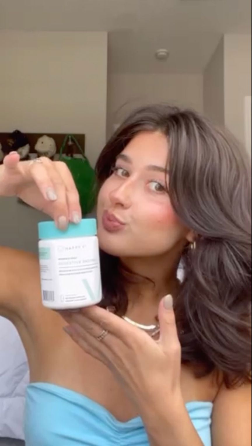 A playfully pouting customer holding a bottle of Happy V Digestive Enzymes in front of her face