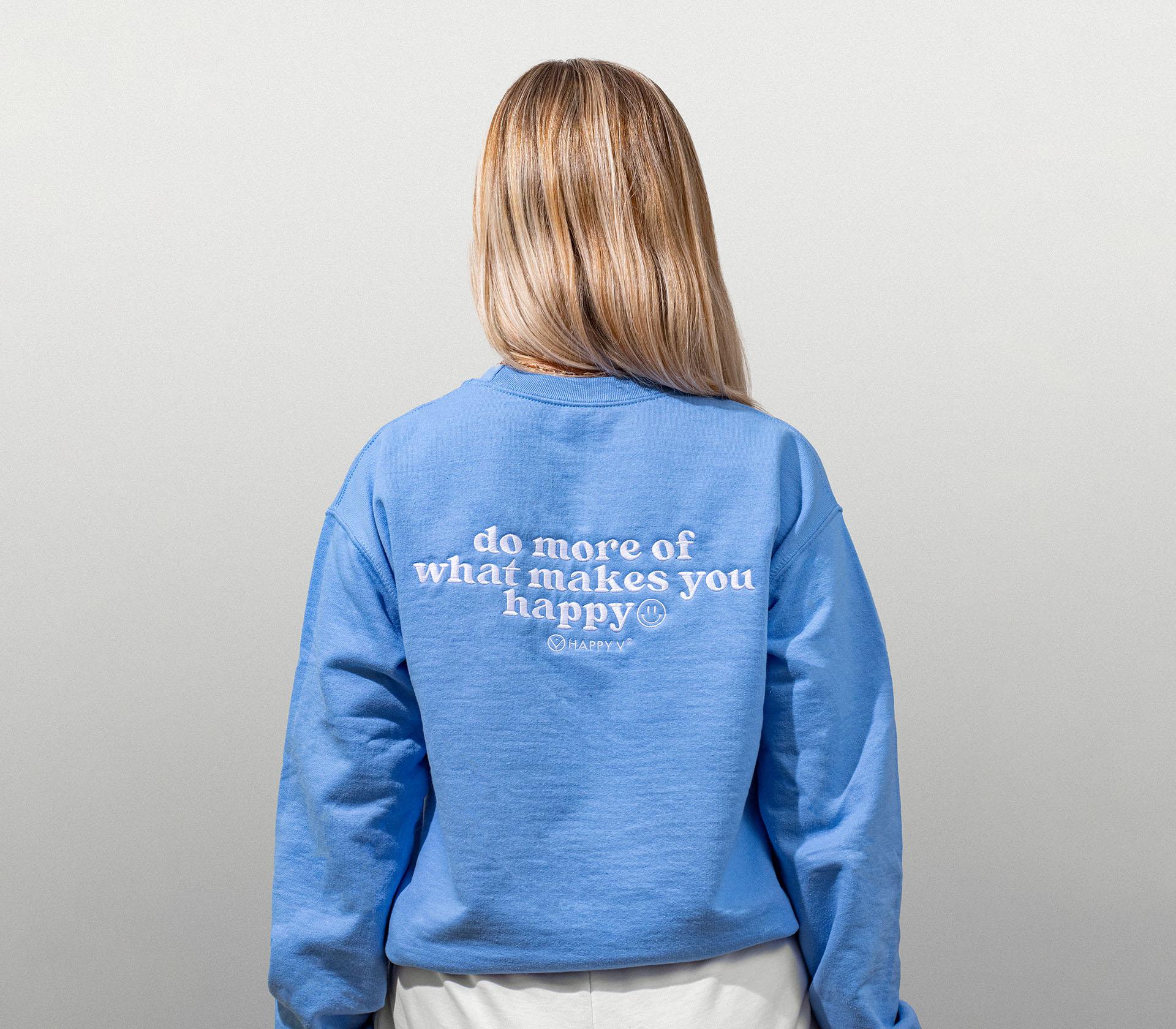 An image showcasing the back of a woman wearing a blue Happy V Crewneck Sweatshirt.