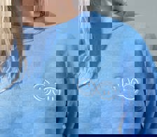 A close up of a woman wearing a blue Happy V Crewneck Sweatshirt, displaying the Happy V logo.